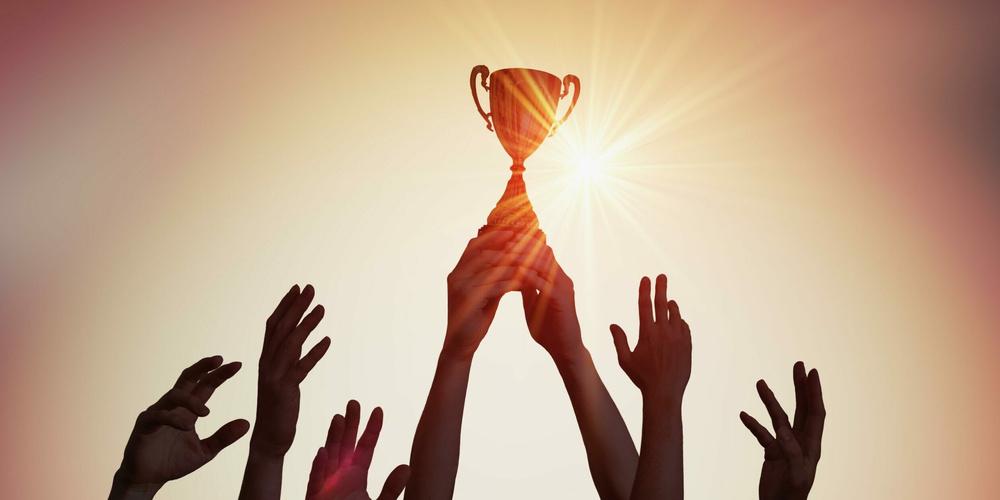 Winning team is holding trophy in hands. Silhouettes of many hands in sunset.